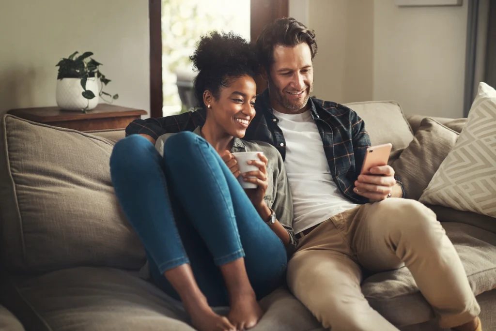 A couple sits on a couch in their living room looking at a phone.